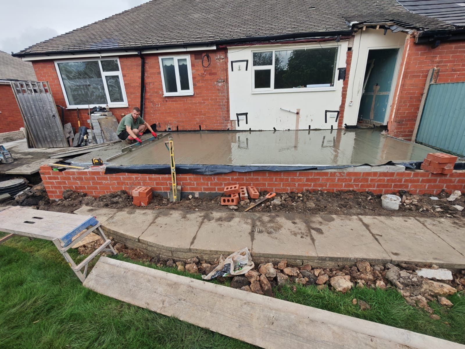 Fresh concrete floor slab being levelled on a new brick base at the back of a bungalow